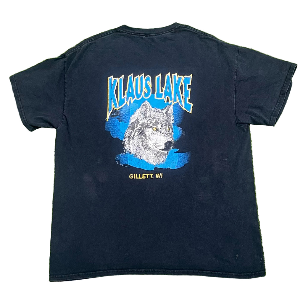 A black short-sleeve t-shirt showing the back graphic with 'KLAUS LAKE' in blue outlined letters above a wolf illustration on a blue shape, and 'GILLETT, WI' below.