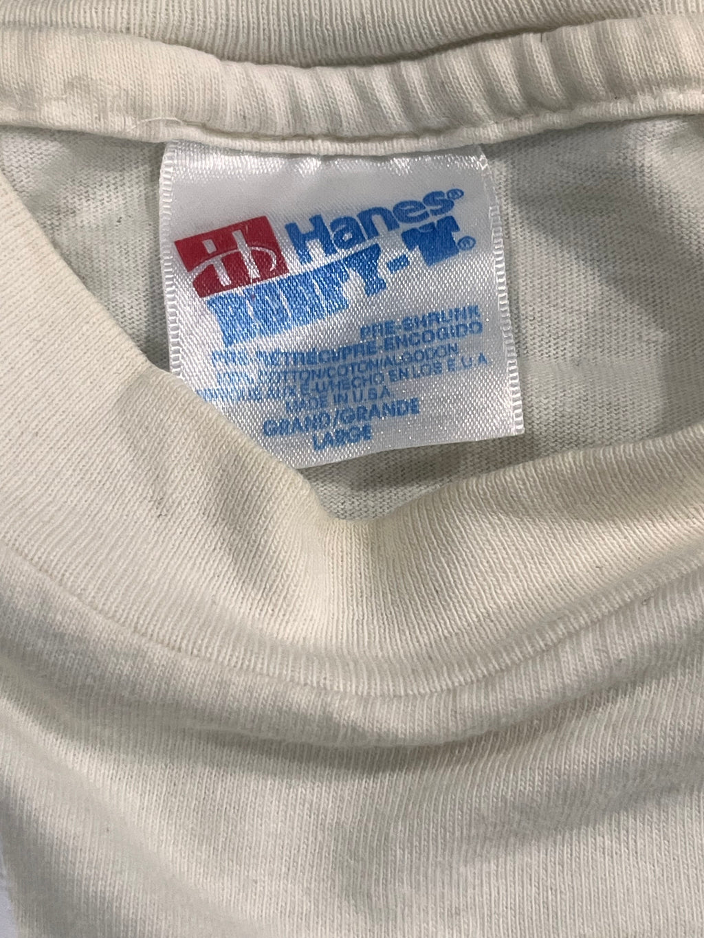 Close-up of a white fabric garment label with blue and red text reading Hanes and Country Store, shown inside a ribbed collar area.