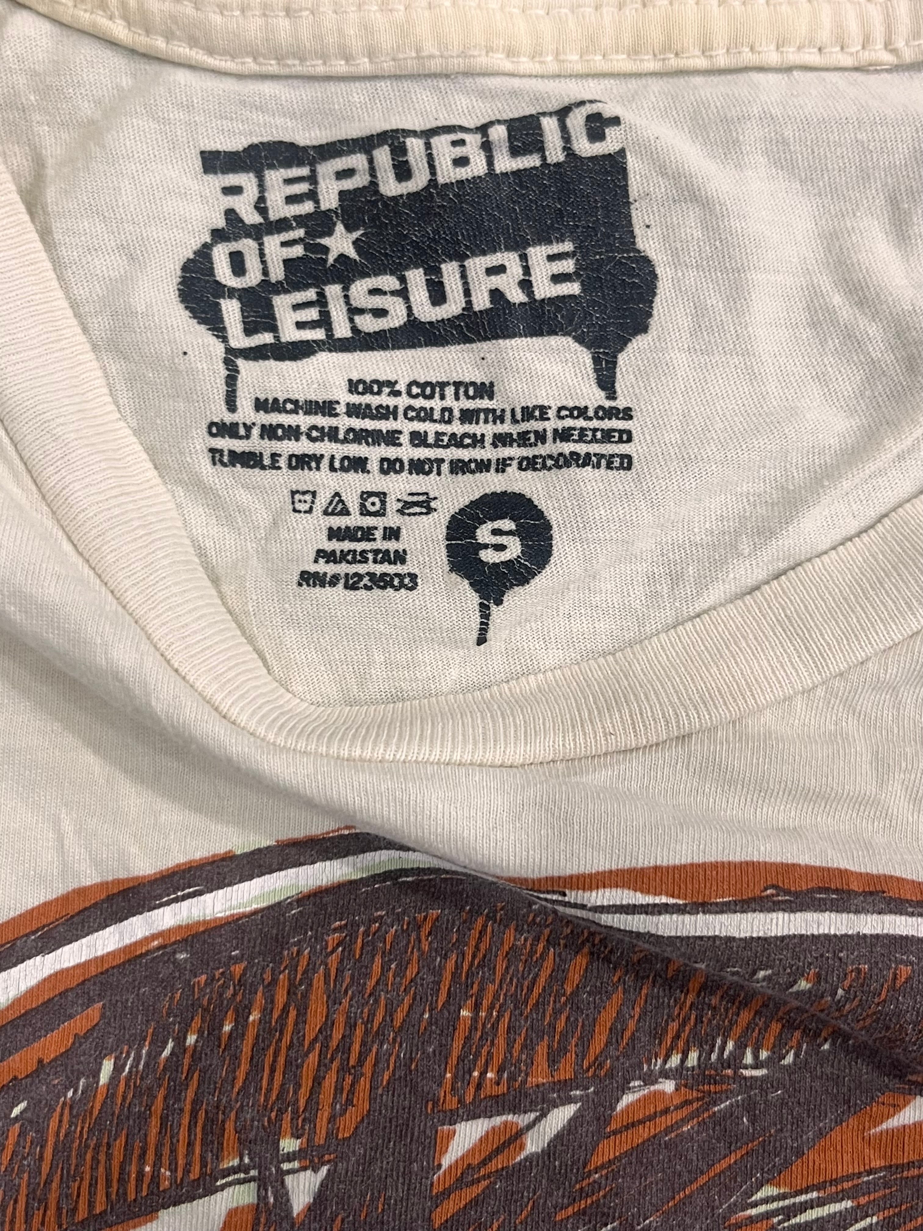 Close-up of the inside collar of a white cotton t-shirt by Republic of Leisure, showing the black printed brand logo, care instructions, and a size label 'S'. The bottom of the shirt features a brown and black graphic print.