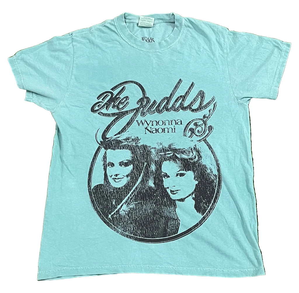 A light blue short-sleeve t-shirt The shirt features a large black distressed print reading 'The Budds' and 'Wyonna Naomi' with a circular portrait graphic of the two women.