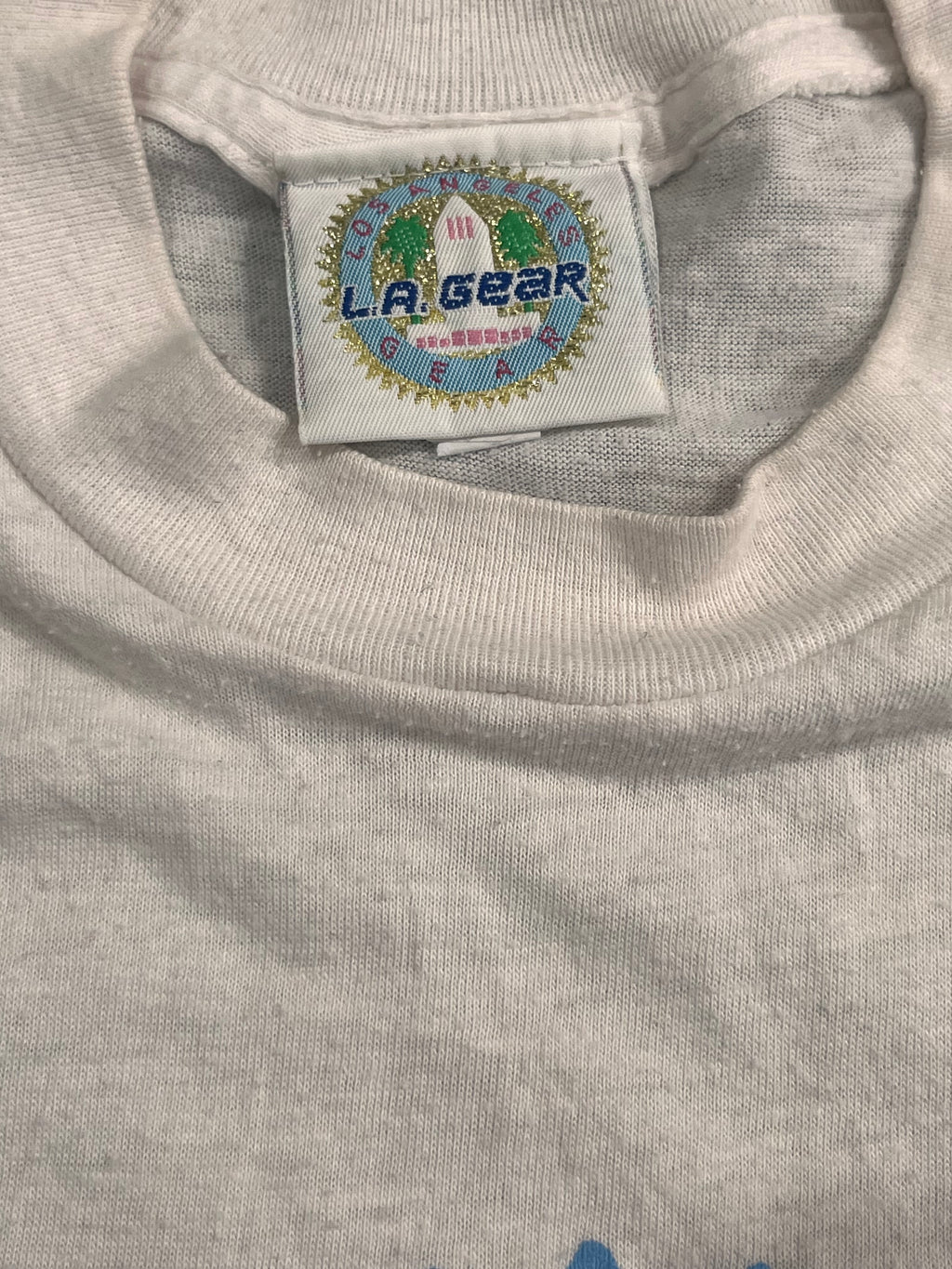 Close-up of a light gray heather crewneck t-shirt showing the inner neck label which reads 'LA GEAR'.