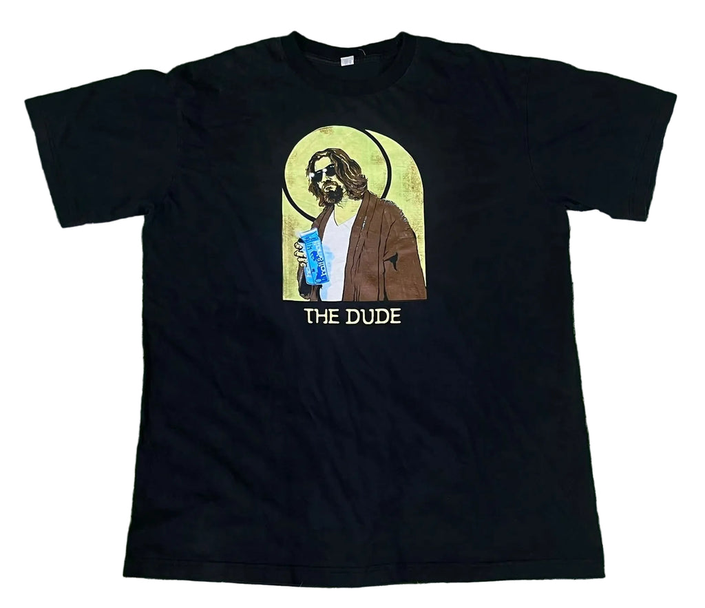 A black short-sleeve graphic t-shirt . The shirt features a central graphic of a bearded man with a halo holding a blue drink, with the text 'THE DUDE' printed below in yellow.