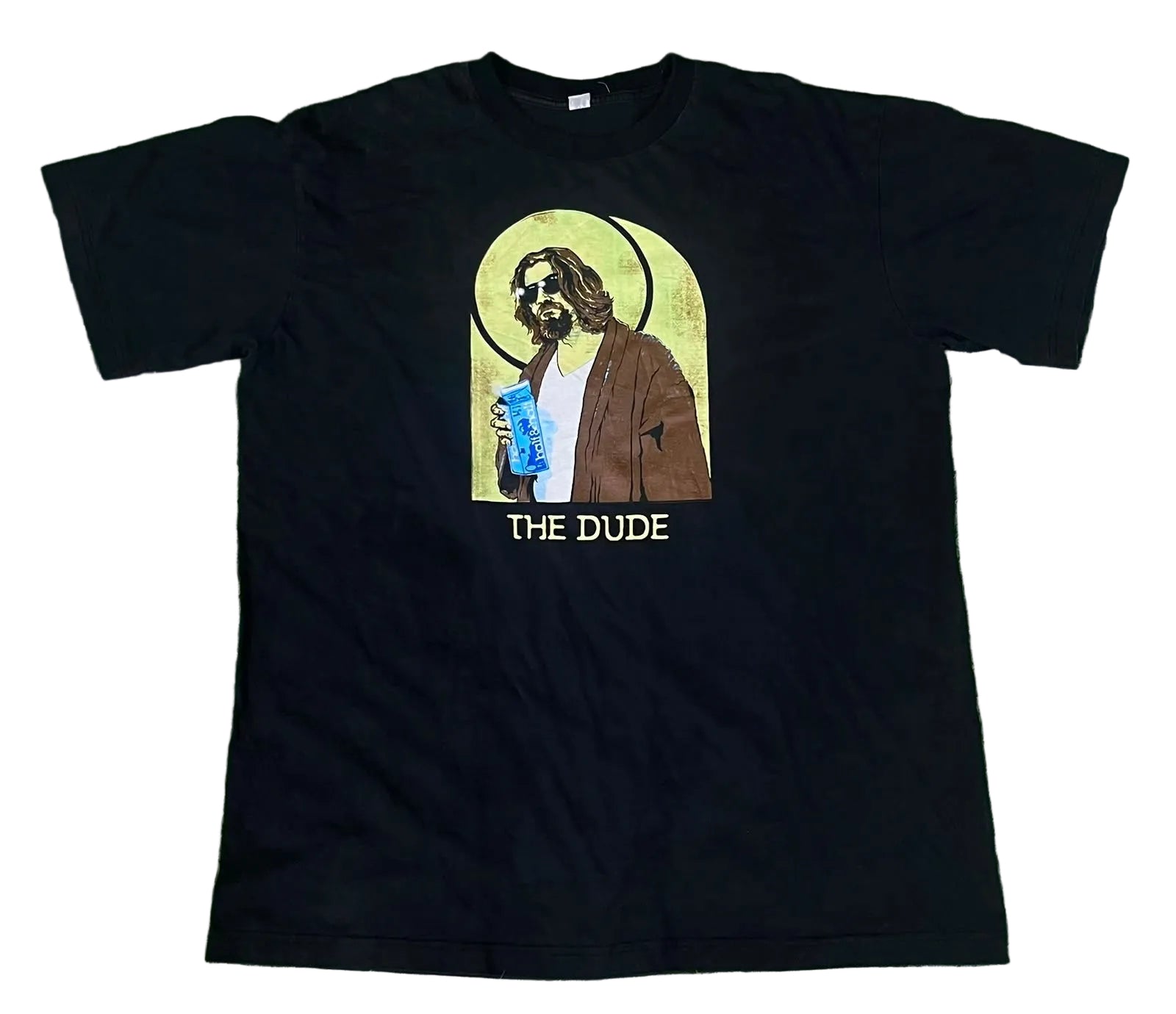 A black short-sleeve graphic t-shirt . The shirt features a central graphic of a bearded man with a halo holding a blue drink, with the text 'THE DUDE' printed below in yellow.