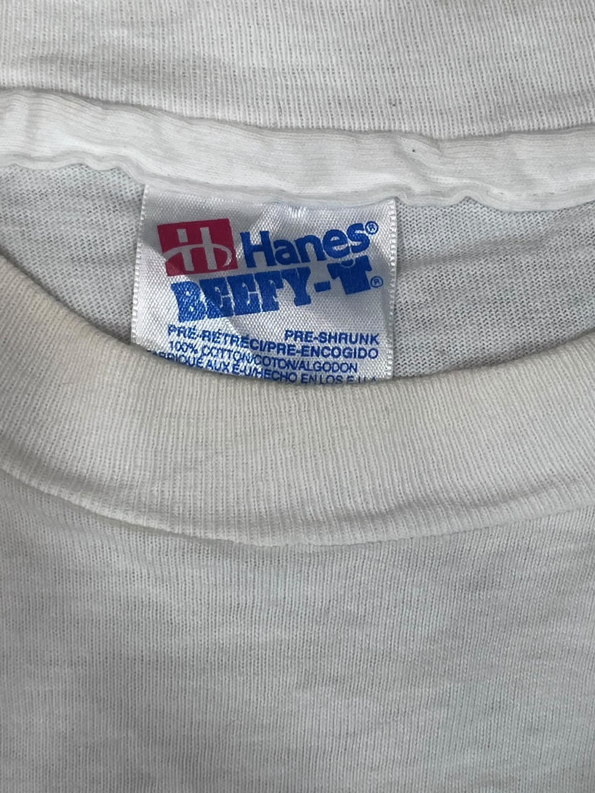 Close-up of the inside collar of a light gray or off-white t-shirt showing the Hanes Beefy-T brand tag.