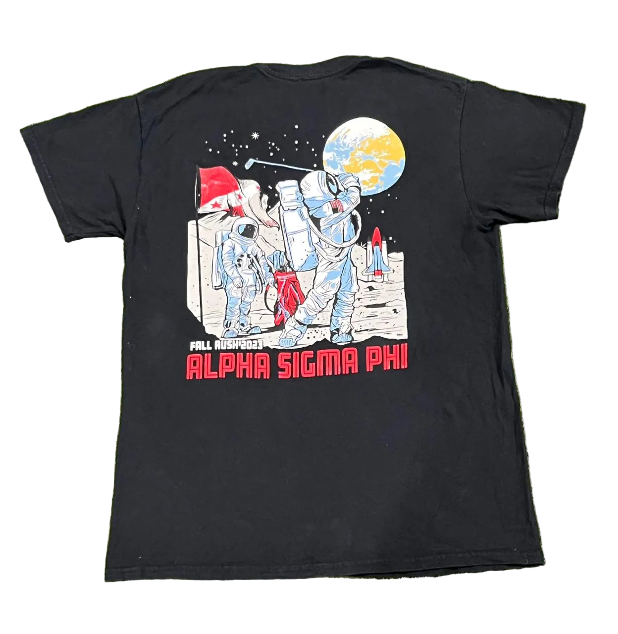A black short-sleeve t-shirt l featuring a large back graphic of astronauts on the moon with a globe and the text 'ALL LEAGUES ARE ALPHA SIGMA PHI' in red.