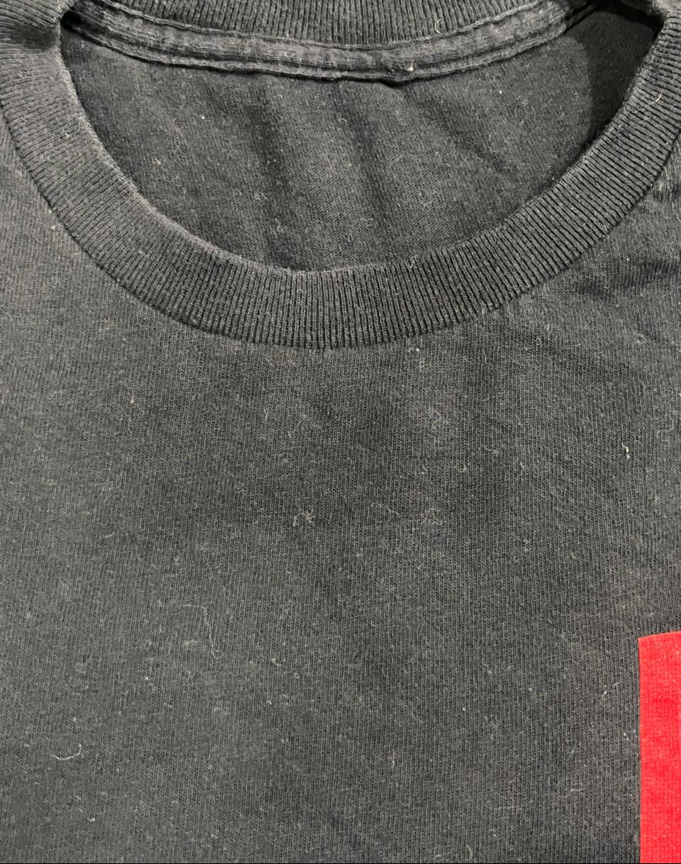 Close-up of a black crewneck t-shirt showing the ribbed collar and a small red graphic on the lower right side,