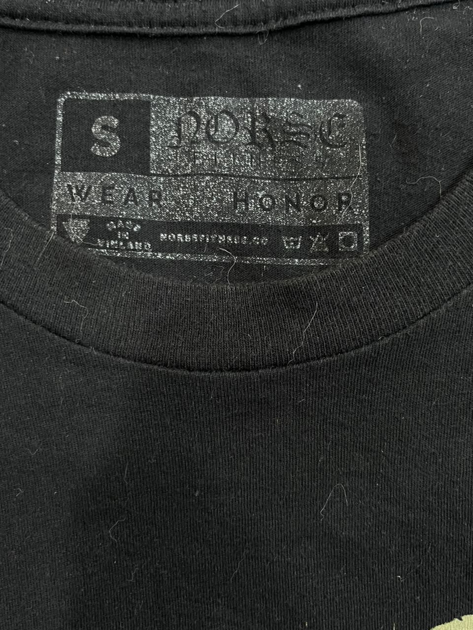 Close-up of the inside neck label of a black t-shirt. The label is printed in a distressed gray font and reads 'SPOIL' and 'WEAR HONOR'.
