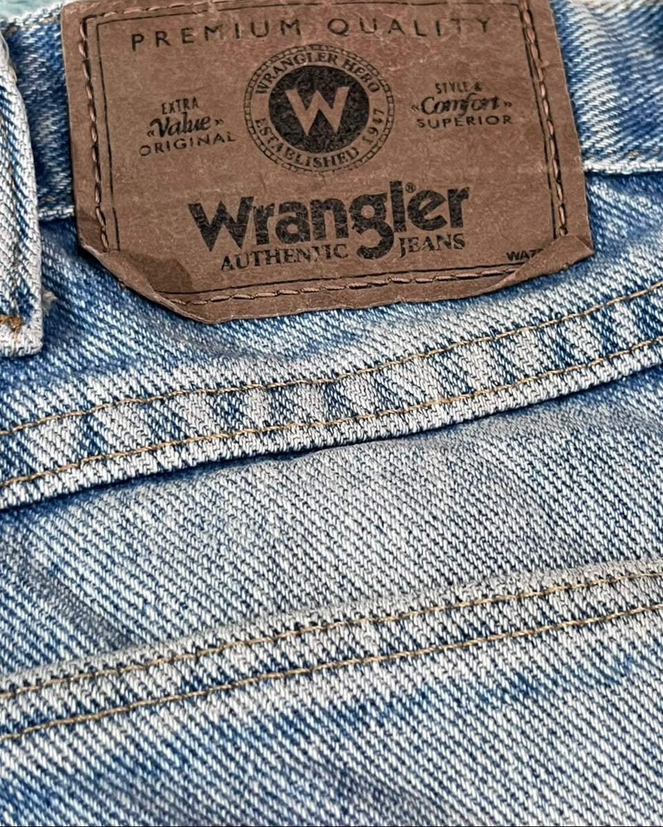 Close-up of a light blue denim jeans waistband showing the brown Wrangler leather brand patch.