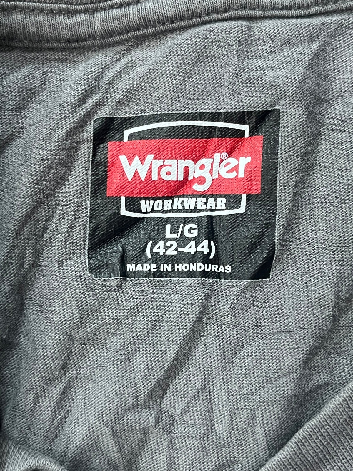 Close-up of a Wrangler Workwear size L/G (42-44) fabric label sewn onto a gray textured garment.