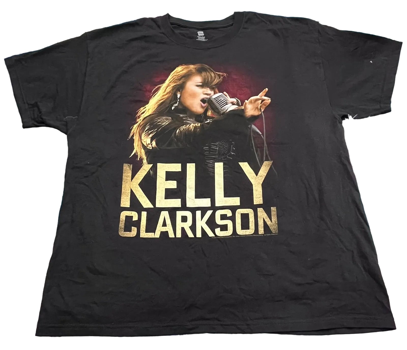 A black short-sleeve graphic T-shirt. The shirt features a large front print of Kelly Clarkson singing into a microphone, with 'KELLY CLARKSON' printed below in large gold letters.