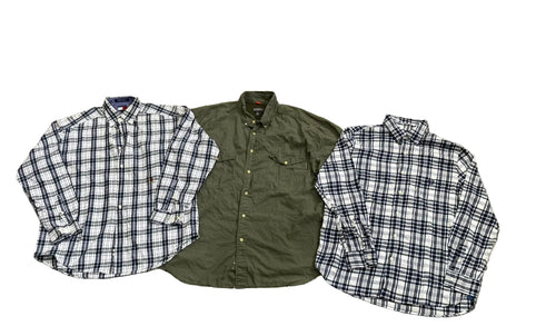 Three folded long-sleeve button-up shirts a white shirt with blue and black plaid on the left, an olive green shirt in the center, and a white shirt with blue and black plaid on the right.