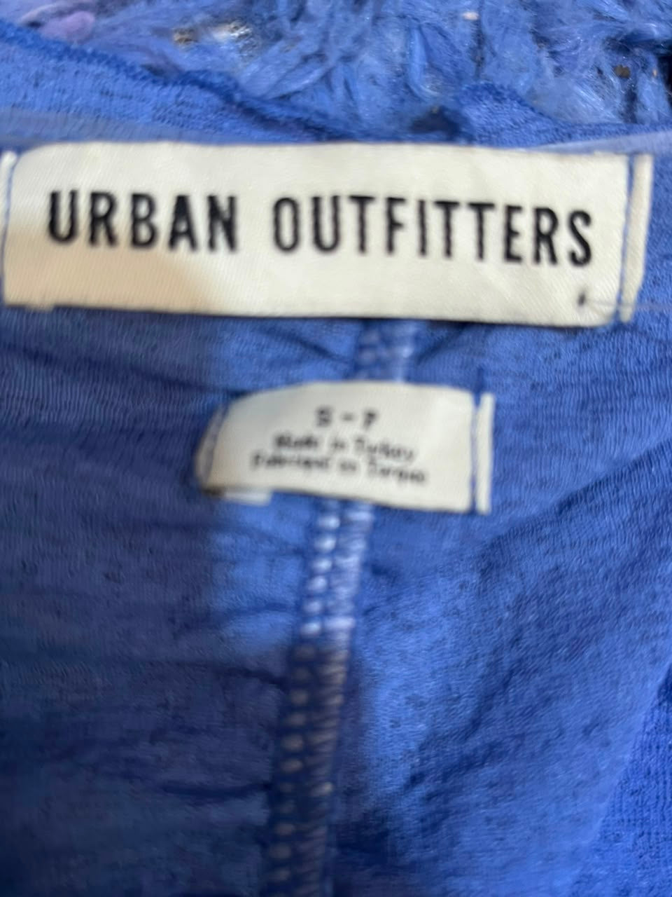 Close-up of a blue garment showing two white fabric labels, with the larger label reading URBAN OUTFITTERS.